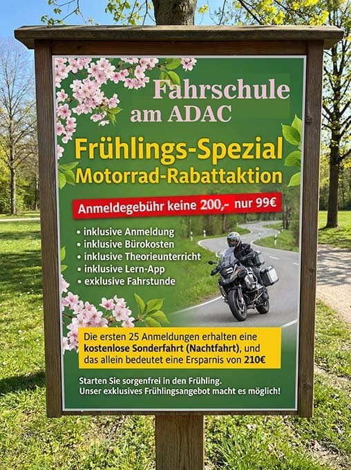 ein schild am straßenrand unter bäumen wirbt für eine frühjahrsaktion einer fahrschule: "motorrad rabattaktion". auf dem schild sind blumen, sonderpreise, eine liste der inbegriffenen dienstleistungen und ein foto einer person auf einem motorrad abgebildet. ein schild am straßenrand unter bäumen wirbt für eine frühjahrsaktion einer fahrschule: "motorrad rabattaktion". auf dem schild sind blumen, sonderpreise, eine liste der inbegriffenen dienstleistungen und ein foto einer person auf einem motorrad abgebildet.